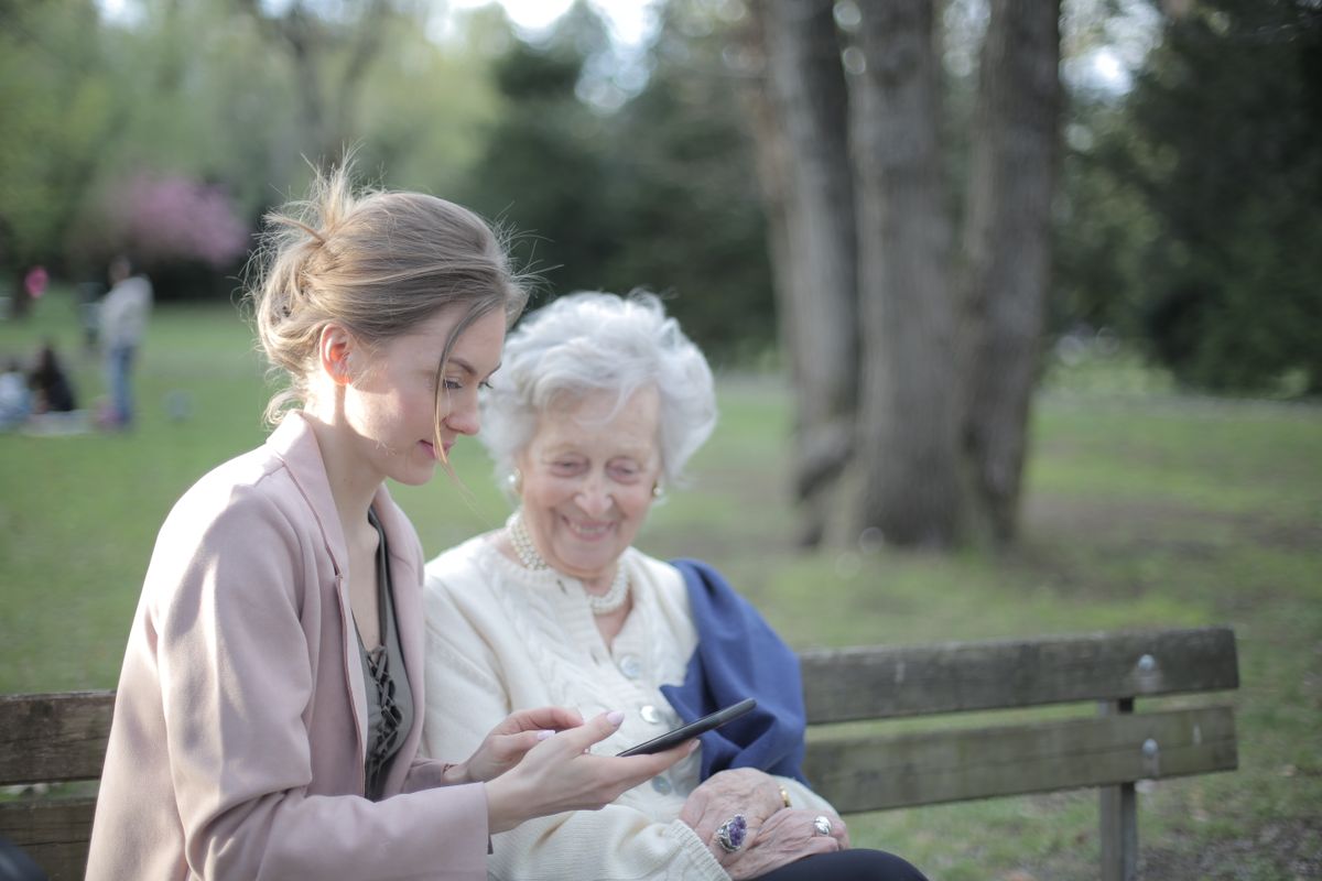 Daughter showing her mother a tablet on a park bench